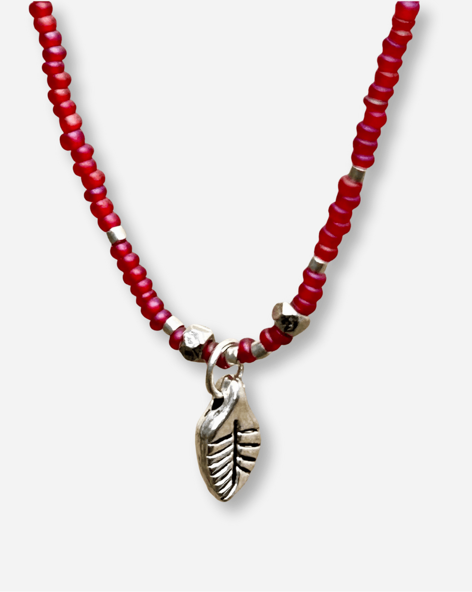 Necklace with red beads and a silver leaf charm on a white background