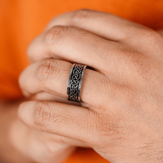Hand wearing a silver ring with intricate design against an orange background