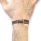Brown leather bracelet with silver anchor charm on a wrist against a white background