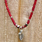 Necklace with red beads and silver leaf charm on a wooden surface