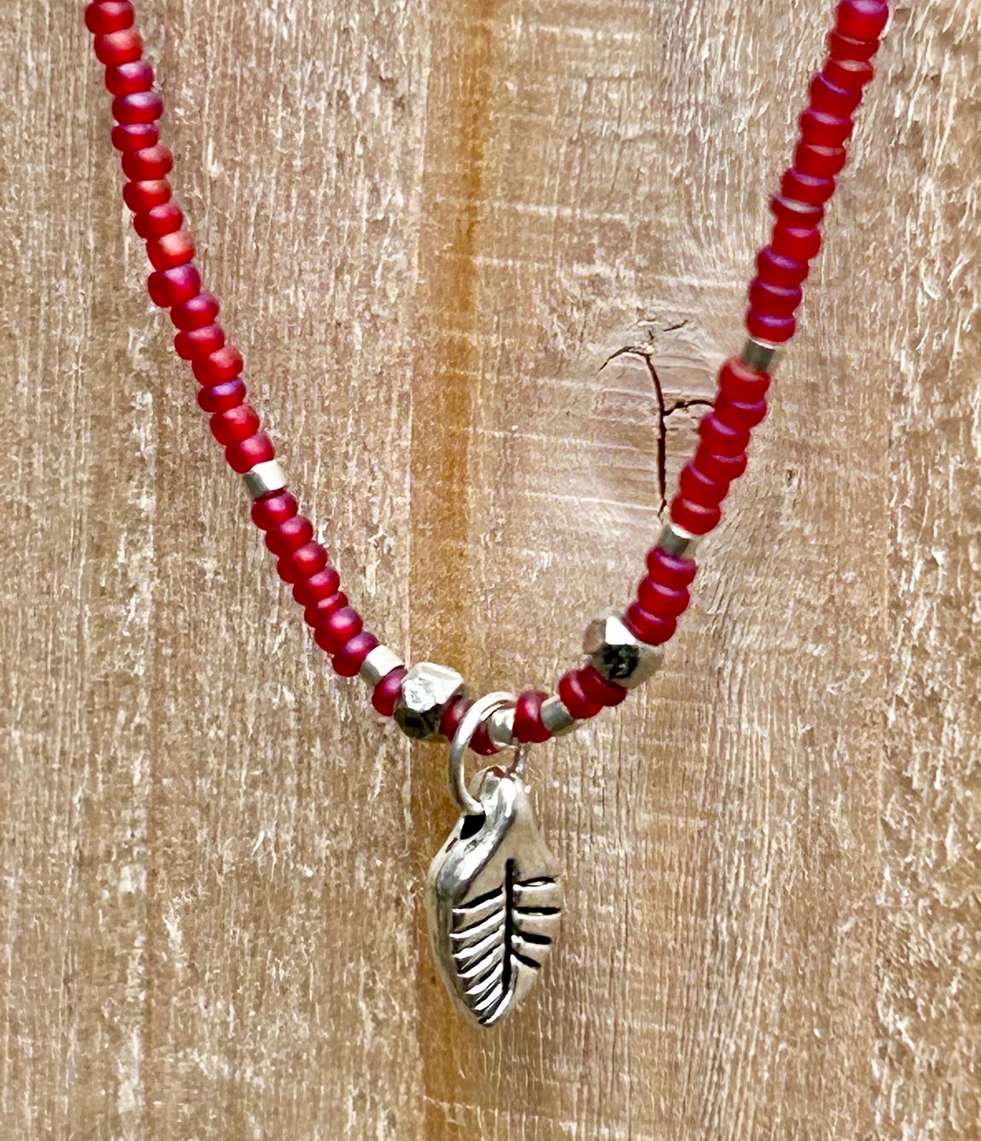 Necklace with red beads and silver leaf charm on a wooden surface