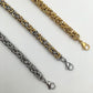 Two chain bracelets, one silver and one gold, on a light gray background.