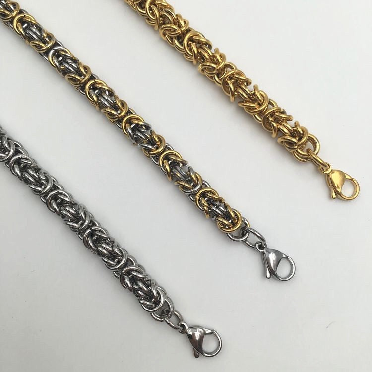 Two chain bracelets, one silver and one gold, on a light gray background.