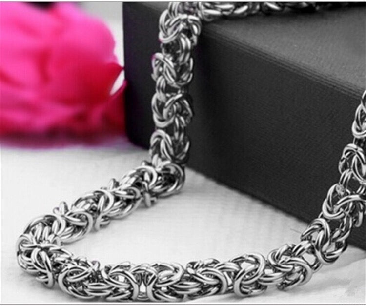 Silver chain necklace on a white surface with a pink flower and black box in the background