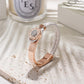 Rose gold bracelet with white leather strap on a textured surface