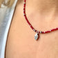 Necklace with red beads and a silver leaf charm worn by a person.