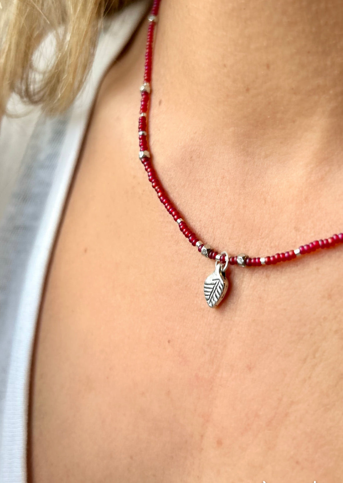 Necklace with red beads and a silver leaf charm worn by a person.