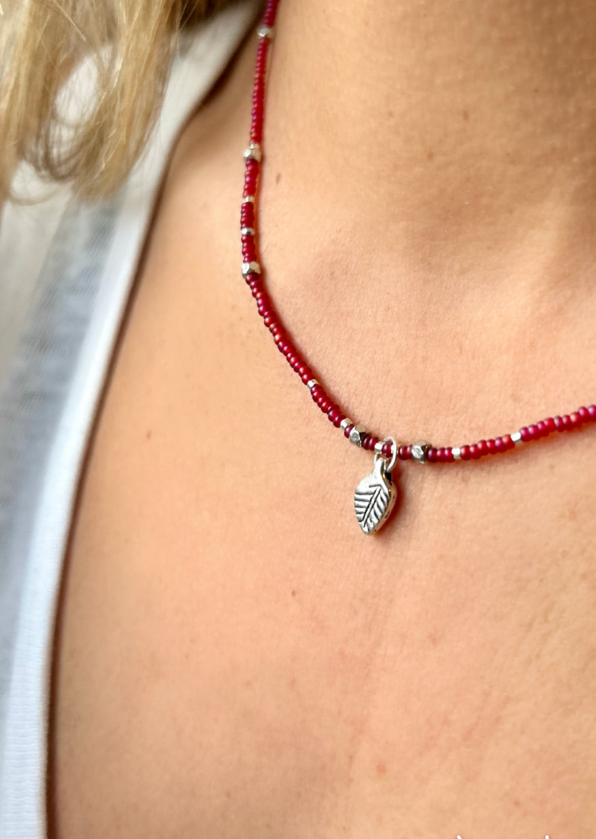 Necklace with red beads and a silver leaf charm worn by a person.