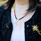 Person wearing a colorful beaded necklace with a moon design, black cardigan, and white turtleneck.