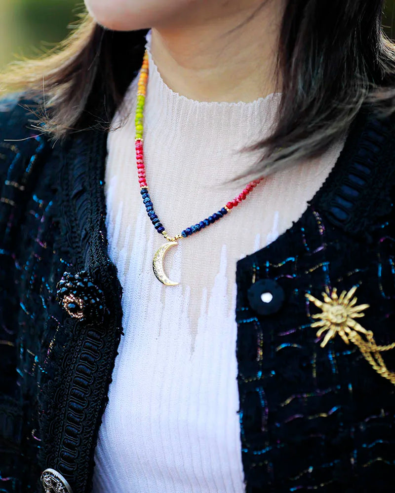 Person wearing a colorful beaded necklace with a moon design, black cardigan, and white turtleneck.