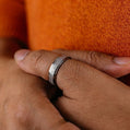 Close-up of a hand wearing a silver ring on an orange fabric background