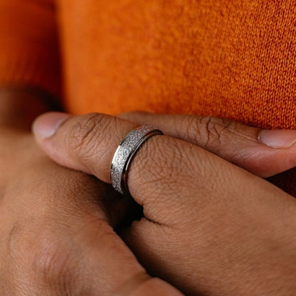 Close-up of a hand wearing a silver ring on an orange fabric background