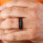 Close-up of a hand wearing a black ring with an orange background