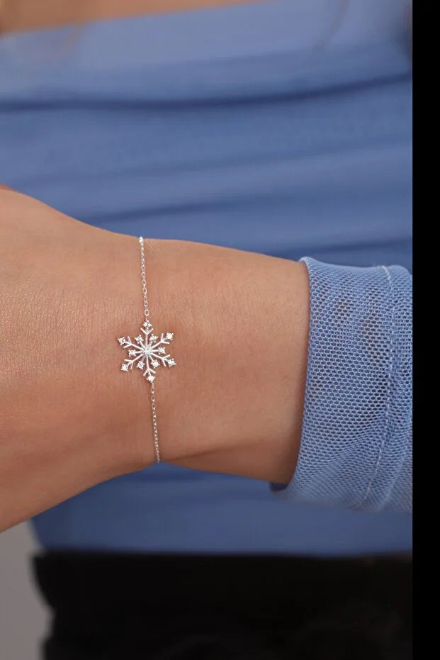 Silver snowflake bracelet on a wrist with a blue sleeve in the background
