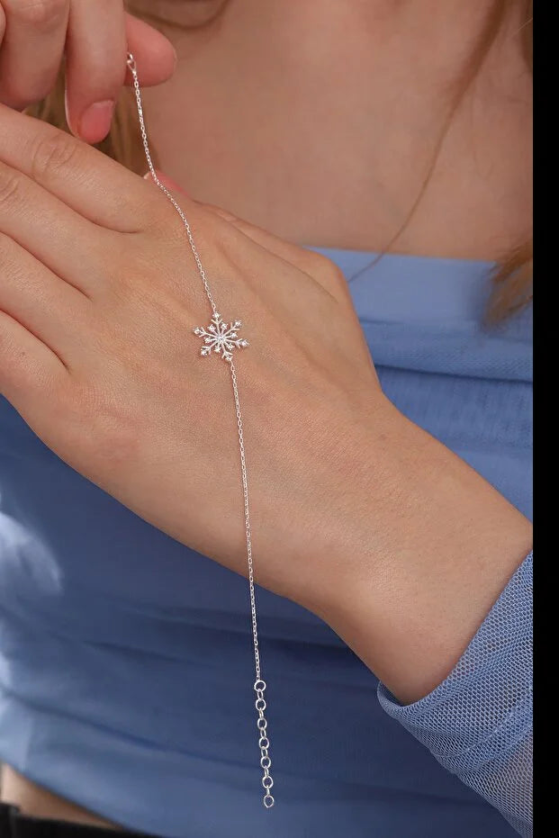 Silver bracelet with a snowflake design on a wrist against a blue background