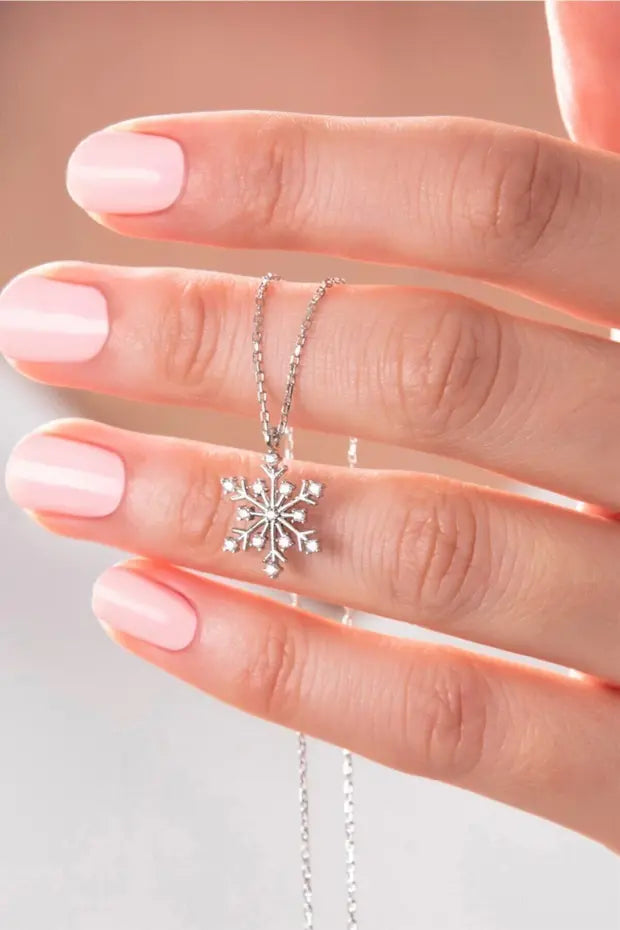 Silver snowflake necklace held between fingers against a neutral background