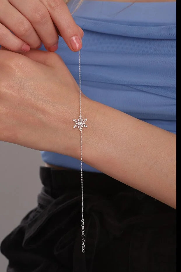 Silver bracelet with a snowflake design on a wrist against a blue and black background