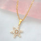 Gold snowflake pendant necklace on a soft pink and gray background
