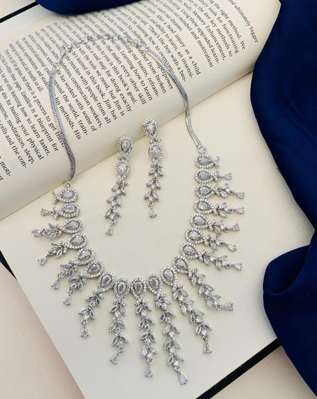 Silver necklace and earrings on an open book with a blue fabric background